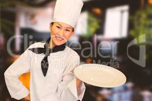 Composite image of smiling female cook holding empty plate in kitchen