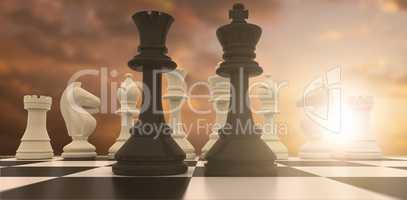 Composite image of black king and queen standing in front of white pieces