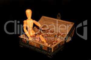 Holzfigur sitzt in Holzkiste mit Geld