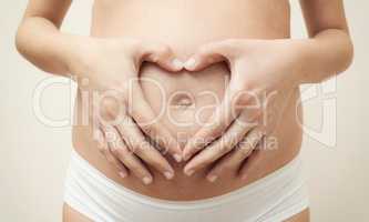 Heart shaped hands of pregnant woman on her belly
