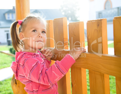 Cute little girl is standing near a fence