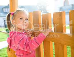 Cute little girl is standing near a fence