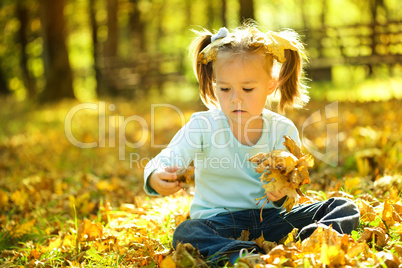 Cute little girl is playing with leaves in park