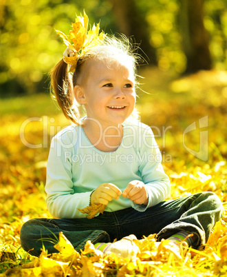 Cute little girl is playing with leaves in park