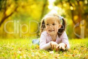 Cute little girl is playing with leaves in park