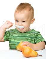 Cute little boy with pears is biting spoon