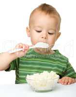 Little boy is eating cottage cheese using spoon