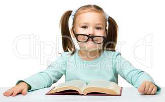 Little girl reads a book while wearing glasses