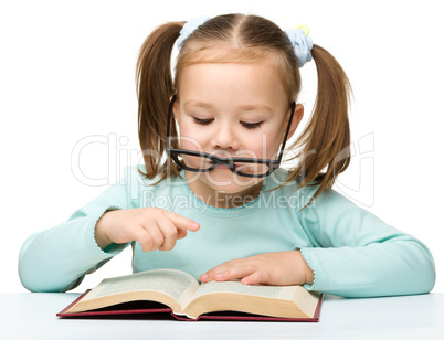 Cute little girl reads a book wearing glasses