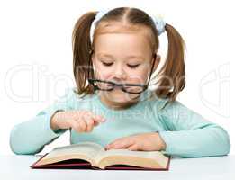 Cute little girl reads a book wearing glasses