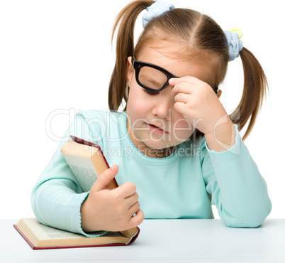 Little girl reads a book while wearing glasses