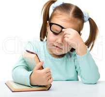 Little girl reads a book while wearing glasses