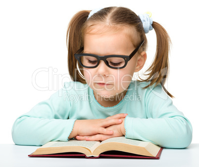 Little girl reads a book while wearing glasses