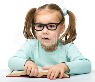 Little girl reads a book while wearing glasses