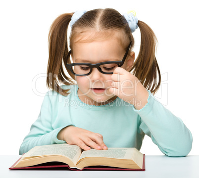 Little girl reads a book while wearing glasses