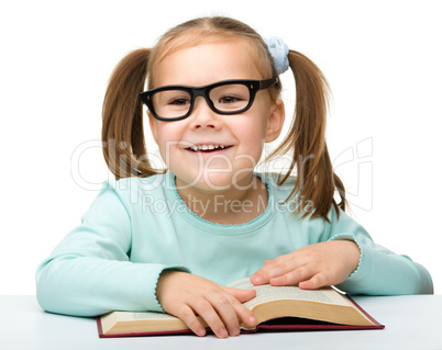 Cute little girl reads a book wearing glasses