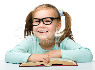 Little girl reads a book while wearing glasses