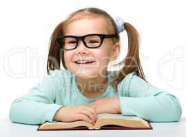 Little girl reads a book while wearing glasses