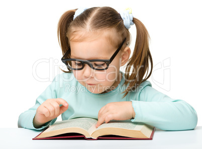 Little girl reads a book while wearing glasses