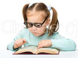 Little girl reads a book while wearing glasses