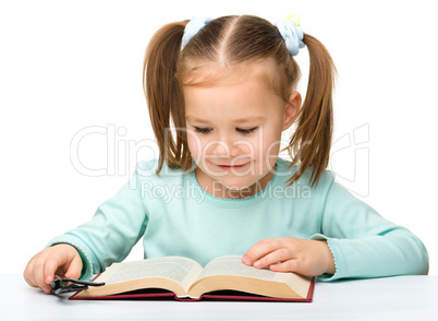 Little girl reads a book while wearing glasses