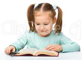 Little girl reads a book while wearing glasses