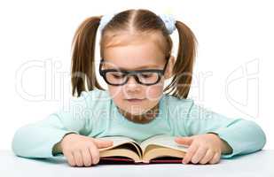 Cute little girl reads a book wearing glasses