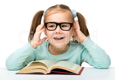 Little girl reads a book while wearing glasses