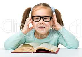 Little girl reads a book while wearing glasses