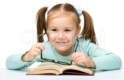 Little girl reads a book while wearing glasses