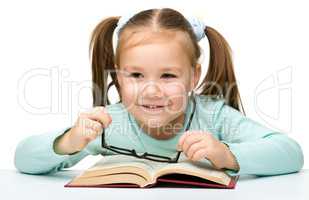 Little girl reads a book while wearing glasses