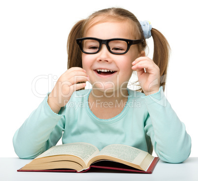 Little girl reads a book while wearing glasses