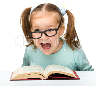 Little girl reads a book while wearing glasses