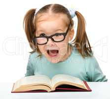 Little girl reads a book while wearing glasses