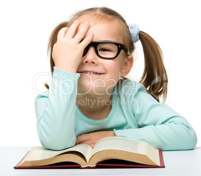 Little girl reads a book while wearing glasses