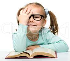 Little girl reads a book while wearing glasses