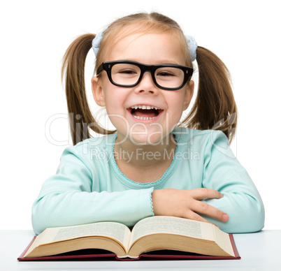 Little girl reads a book while wearing glasses