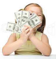 Cute little girl is covering her eyes with dollars
