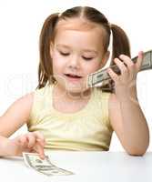 Cute cheerful little girl is counting dollars