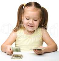 Cute cheerful little girl is counting dollars