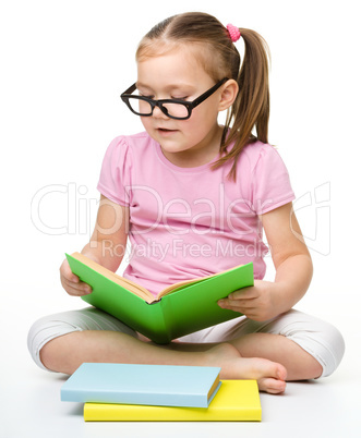 Cute little girl reads a book wearing glasses