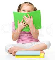 Cute little girl is hiding behind a book