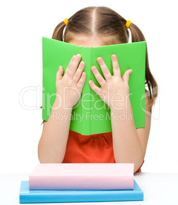 Cute little girl is hiding behind a book