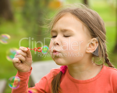 Cute little girl is blowing soap bubbles