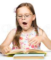 Cute little girl is yawning while reading book