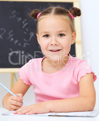 Little girl is writing using a pen