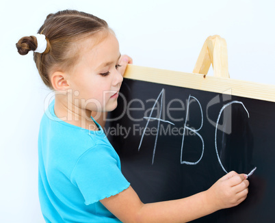 Little girl is writing on a blackboard