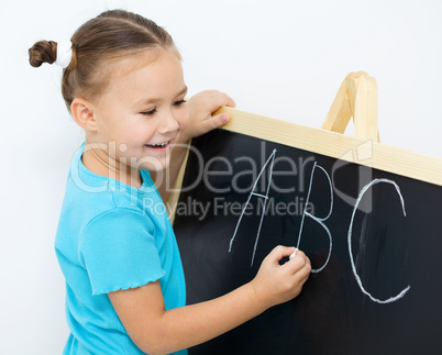 Little girl is writing on a blackboard