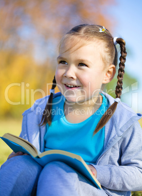 Little girl is reading a book outdoors