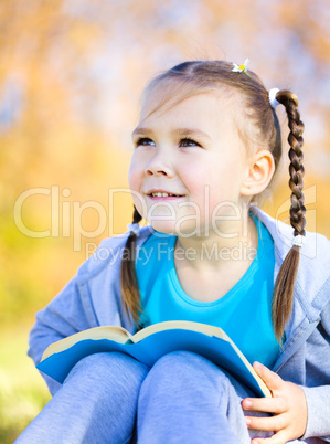 Little girl is reading a book outdoors